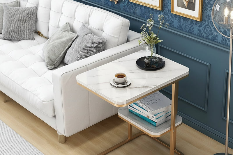 A white marble topped coffee table with a gold frame, positioned on a wood floor in a living room setting, with a cup of coffee and a book on top of the table.